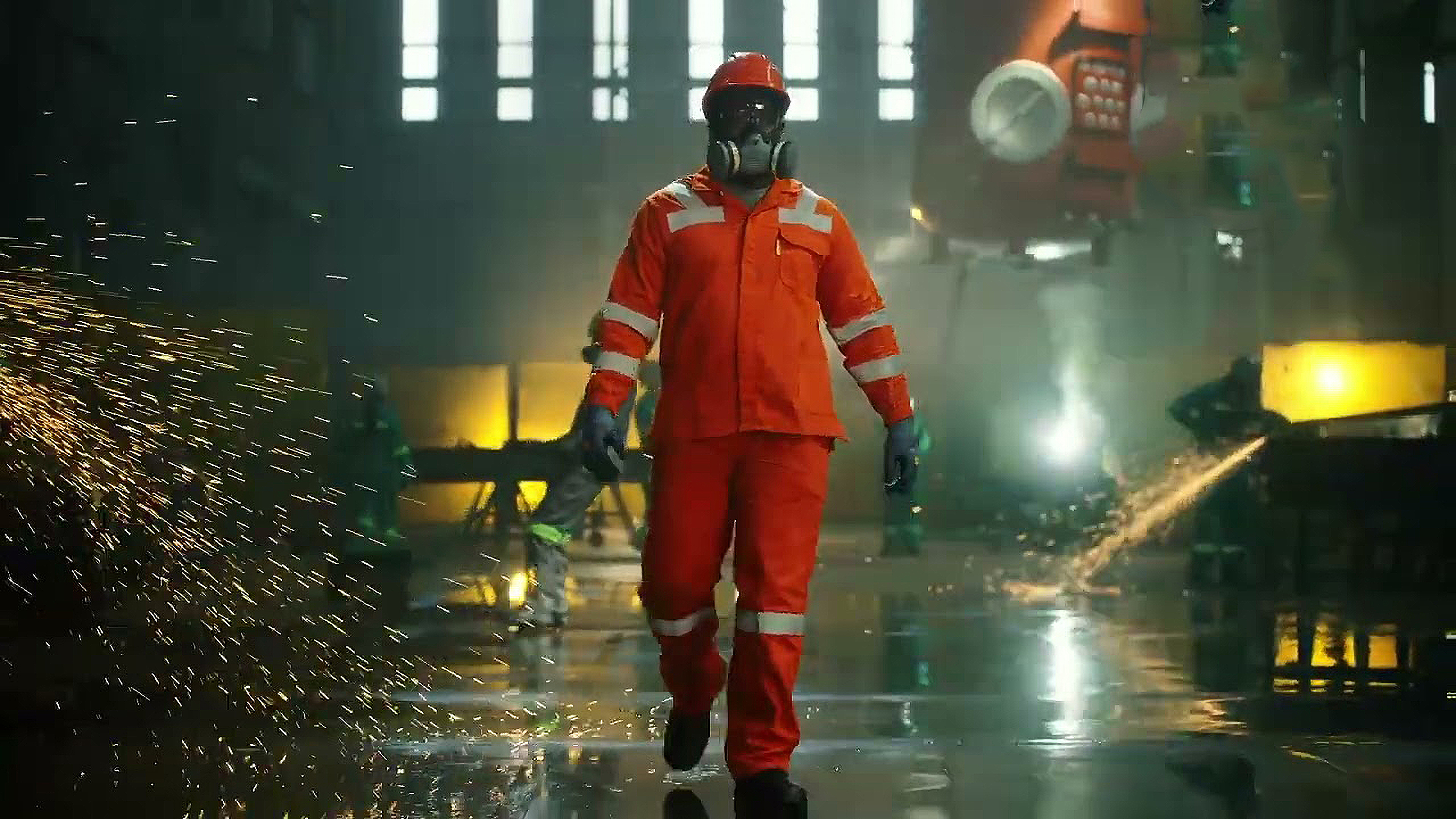 Worker in orange protective coverall, hard hat and respirator walking through an industrial foundry